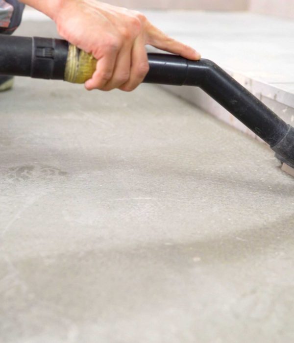 A worker vacuums the concrete floor. Cleaning of construction waste with a vacuum cleaner. Worker vacuuming debris and dust from floor after drilling concrete wall.