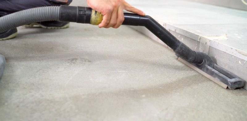 A worker vacuums the concrete floor. Cleaning of construction waste with a vacuum cleaner. Worker vacuuming debris and dust from floor after drilling concrete wall.