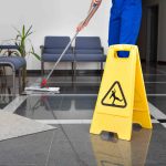 Close-up Of Man Cleaning The Floor With Yellow Wet Floor Sign