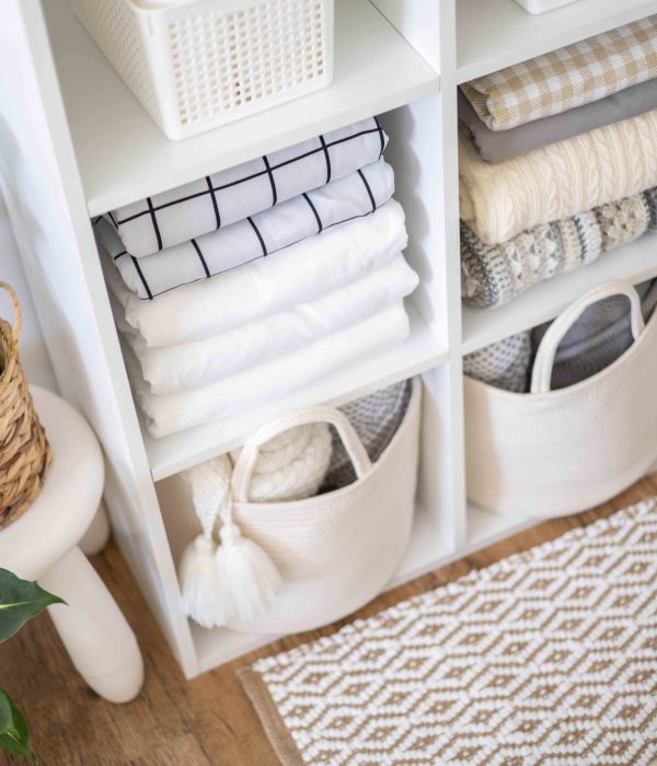 Neatly folded linen cupboard shelves storage at eco friendly straw basket placed closet organizer drawer divider. Stacks towels pillows plaids soft sheets bedding cabinet filling Nordic organization