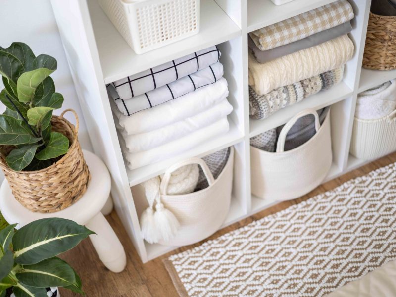 Neatly folded linen cupboard shelves storage at eco friendly straw basket placed closet organizer drawer divider. Stacks towels pillows plaids soft sheets bedding cabinet filling Nordic organization